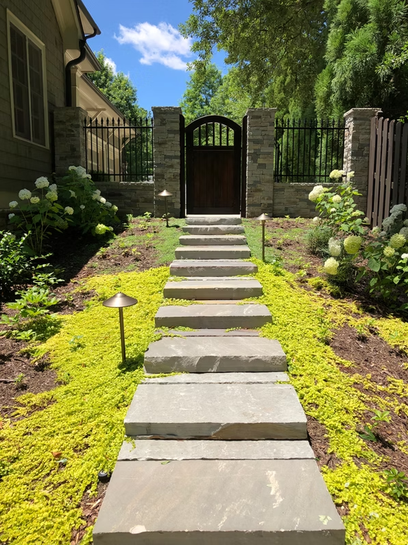 Stone walkway lined with hydrangeas leading to a garden gate